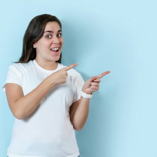 Young woman over isolated blue background pointing finger to the side.